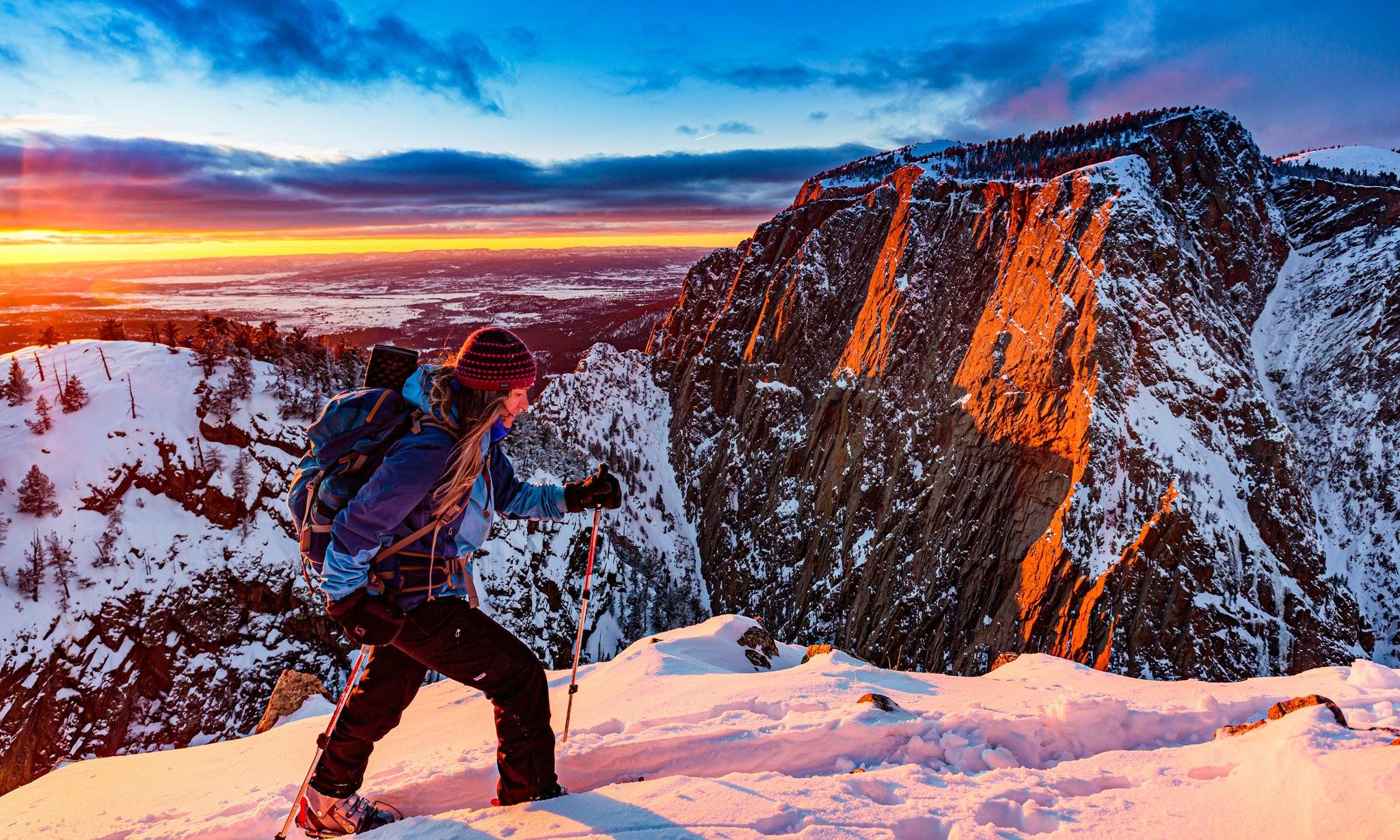 Una persona asciende con raquetas hacia un filo nevado al amanecer, con el cielo encendido