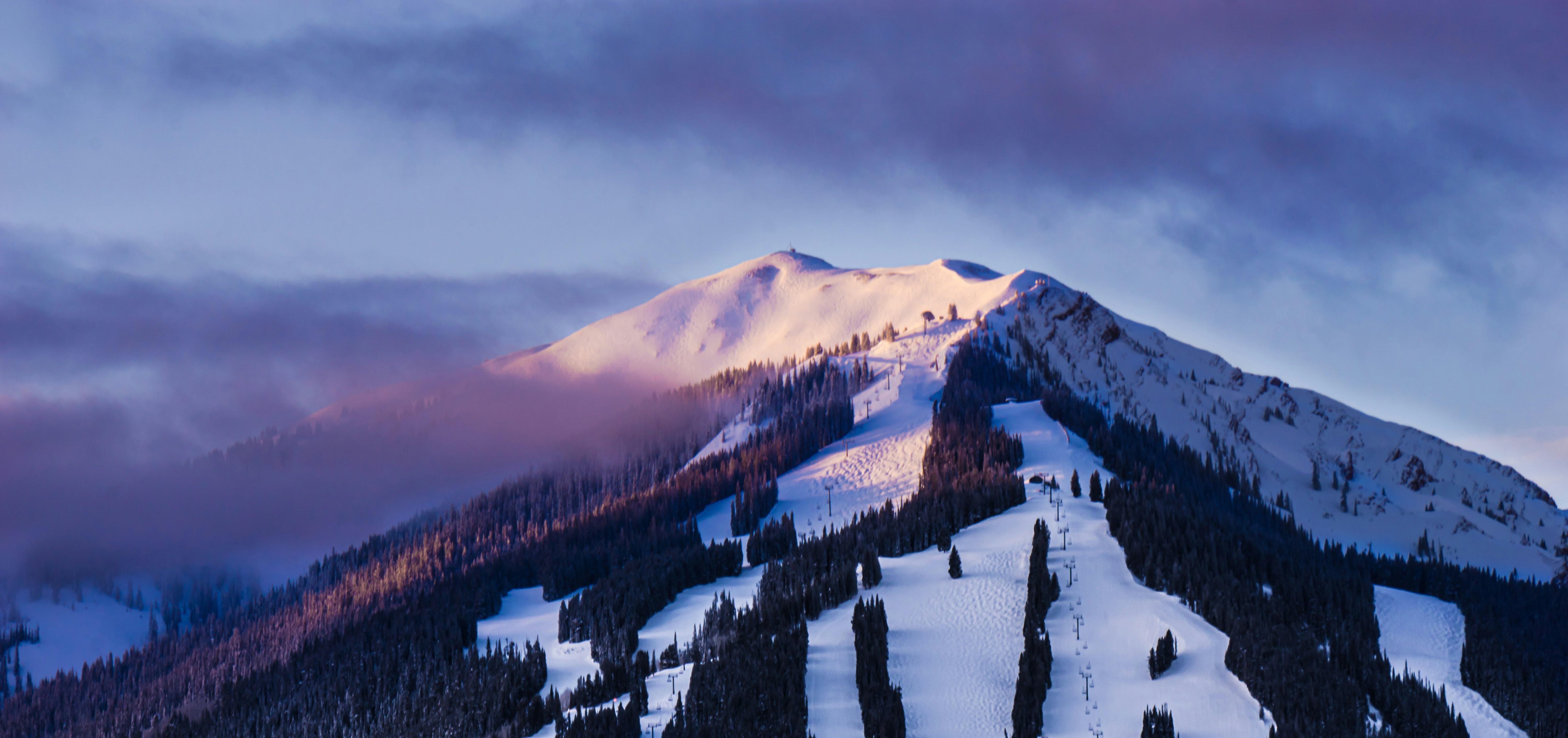 La cumbre de Park City encendida de rosa y violeta al amanecer, con las pistas y los medios de elevación