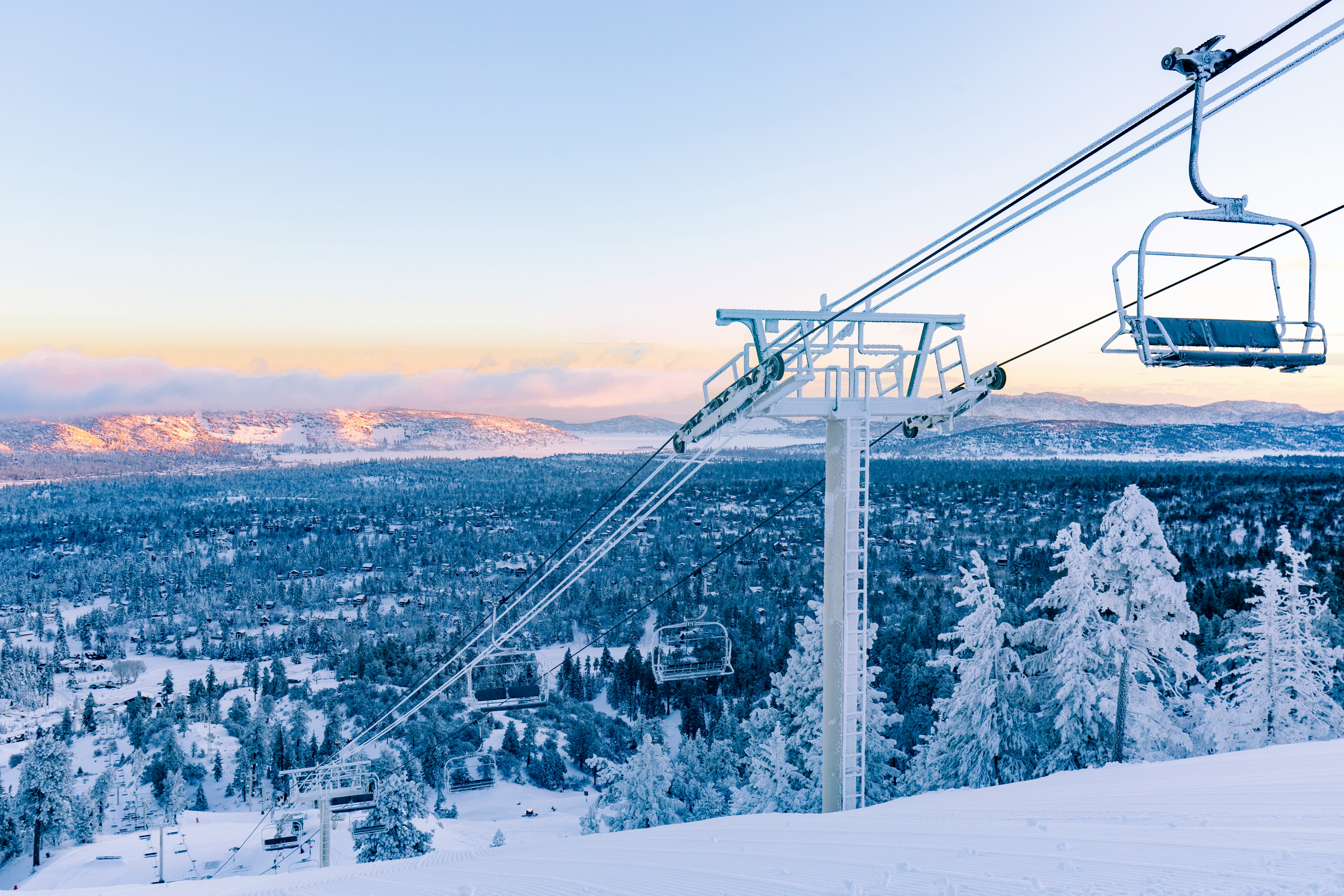 Una silla de un telesilla cubierta de escarcha al amanecer, sobre el bosque nevado