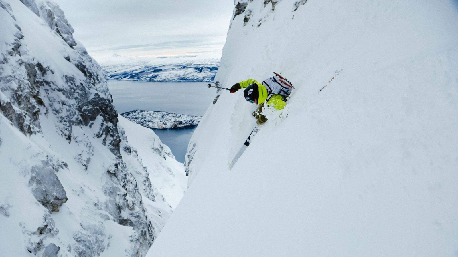 Esquiador descolgándose por un couloir empinado sobre un fiordo helado